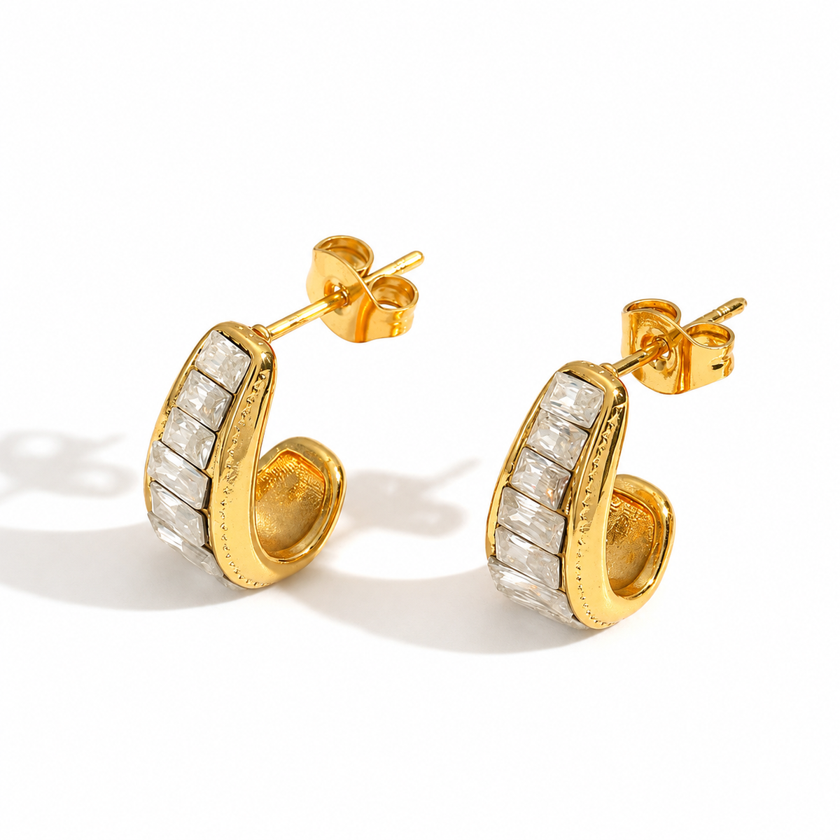 Small gold hoop earrings featuring a curved design set with a row of rectangular clear crystals