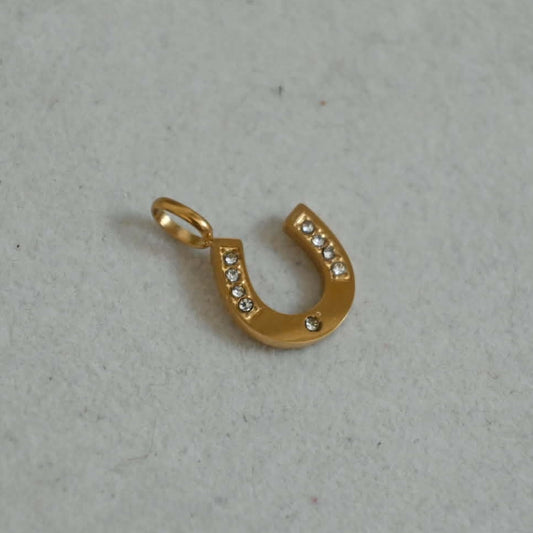 Gold horseshoe charm with small crystal details on a neutral background, designed for charm bracelets and necklaces